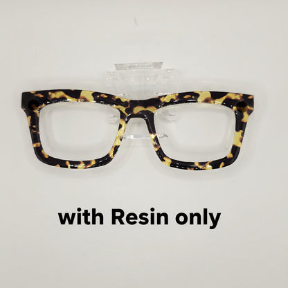 Tortoiseshell eyeglasses with a glossy black, brown, and yellow mottled pattern, displayed on a clear plastic stand against a light gray background.